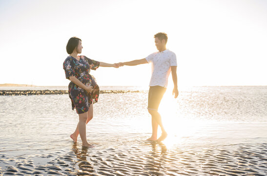 Pregnant couple walking on beach at sunset