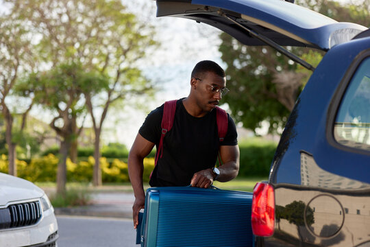 Young black male tourist putting luggage into car