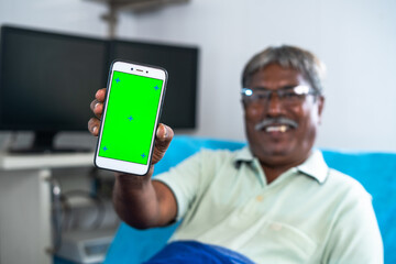 Focus on mobile phone Happy patient showing green screen mobile phone by looking at camera at hospital ward - concept of health care service, app advertisement and treatment