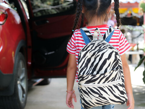 Rear view of happy smiling little girl with backpack getting in the car to ride to school. Little girl is happy and ready to learn. Back to school.
