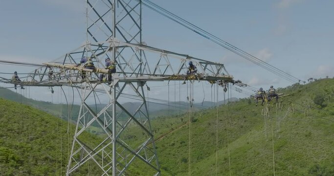 Aerial flying near unrecognizable people working on high voltage tower cables