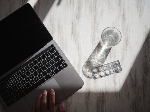 Still-life shot with laptop, pills and glass of water