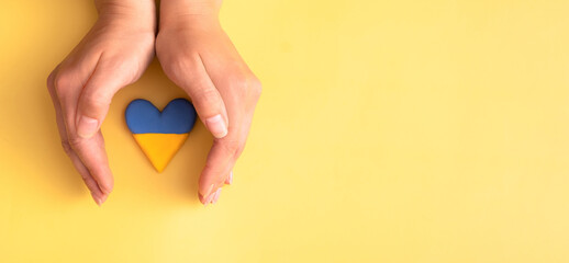 Female hands holding over heart in Ukrainian yellow and blue colors flag on colored background banner format