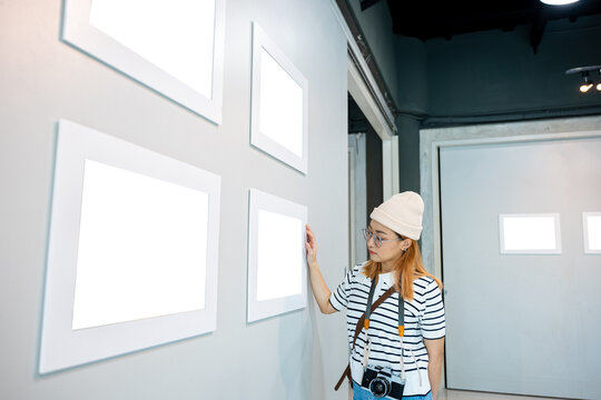 Asian woman hold camera at art gallery collection in front framed paintings pictures on wall and looking, Photographer visit at photo frame to leaning against at show exhibit artwork gallery picture