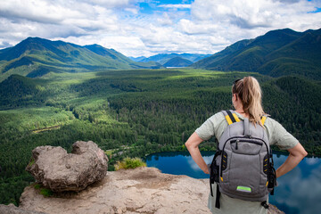 View from behind of a female hiker standing on the top of a mountain overlooking a beautiful scenic rocky mountain landscape and a lake. Gorgeous view from above