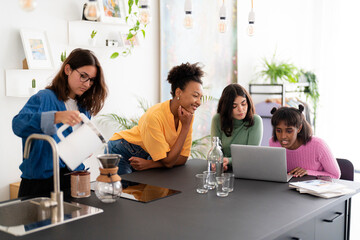 Diverse women working on laptop at kitchen counter