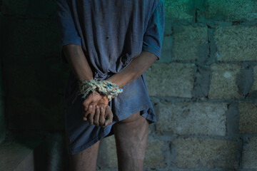 A young dirty man in tattered clothes is locked in a concrete basement