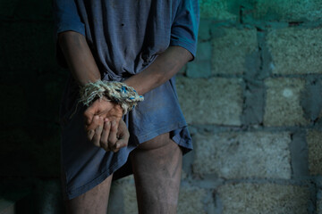 A young dirty man in tattered clothes is locked in a concrete basement