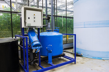 Electric motor water pump at greenhouse. Interior and equipment with pipelines and water tank in...