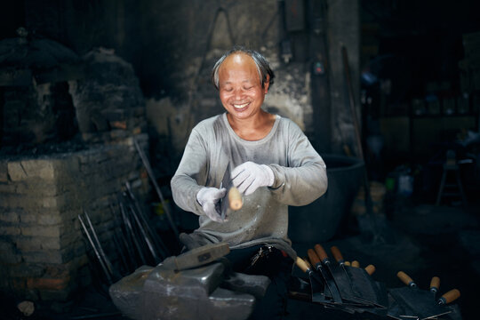 An East Asian Ironworker manufactures a Chinese kitchen knife.