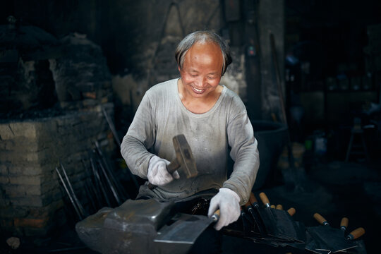 An East Asian Ironworker manufactures a Chinese kitchen knife.