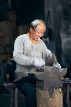 An East Asian Ironworker manufactures a Chinese kitchen knife.