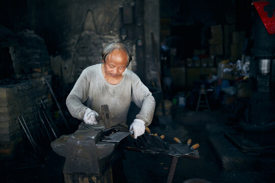 An East Asian Ironworker manufactures a Chinese kitchen knife.