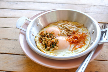 Pan-fried eggs with toppings on the wooden table.