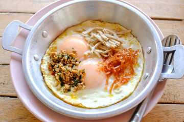 Pan-fried eggs with toppings on the wooden table.