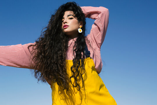 Young girl with long black curly hair posing under the blue sky