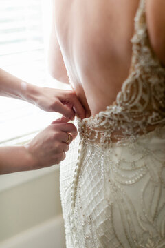 Closeup of Woman Fastening the Back of a Bride's Dress