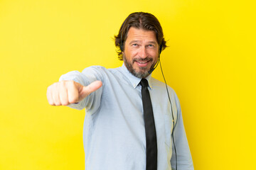 Telemarketer dutch man working with a headset isolated on yellow background giving a thumbs up gesture