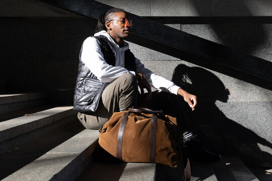 Stylish black man sited in the stairs with a hard morning sunlight 