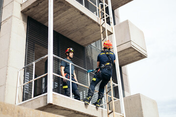 Firefighters climbing a building with a harness and ladder