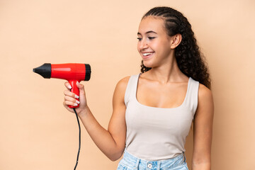 Young woman holding a hairdryer isolated on beige background with happy expression