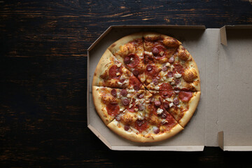 Pizza in a cardboard box against a dark background. View from above. Pizza delivery.
