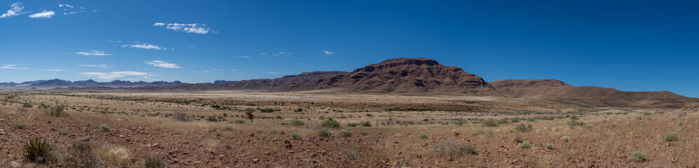 Fototapeta na wymiar A panoramic photo of a hill/mountain in the middle of Namibia. Blue sky with scattered blue clouds.
