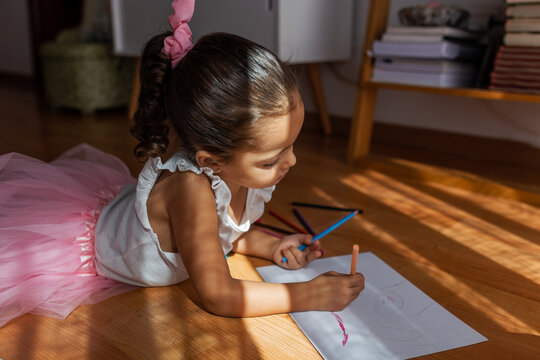 little girl dressed as a ballerina coloring a drawing at home