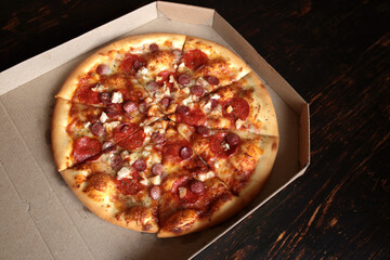 Pizza in a cardboard box against a dark background. View from above. Pizza delivery.