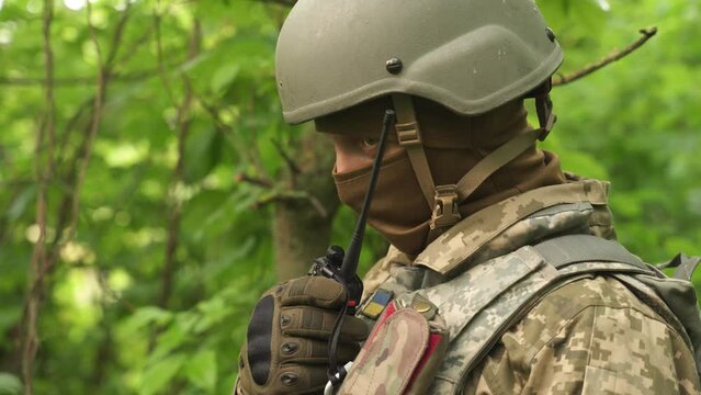 a portrait of a Ukrainian military man communicating by radio. a military man in the forest reports news on a walkie-talkie and gives orders. communication between units during a combat mission