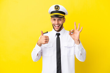 Airplane caucasian pilot isolated on yellow background showing ok sign and thumb up gesture