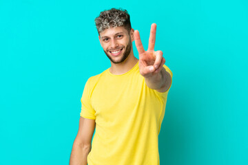 Young handsome caucasian man isolated on blue background smiling and showing victory sign