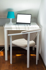 Home office with open laptop, lamp, table and chair