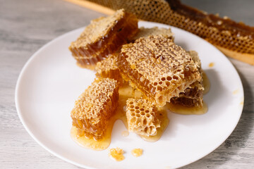 Pieces of sweet honeycomb on the white plate near the open honeycomb in wooden frame on the table