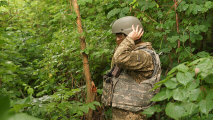 Ukrainian military man in combat positions adjusts the tactical helmet on his head. protective equipment of the soldier. an infantryman in the forest during a military operation