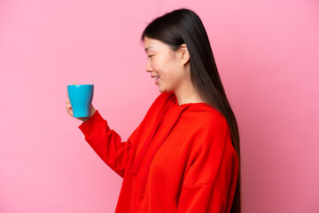 Young Chinese woman holding cup of coffee isolated on pink background with happy expression