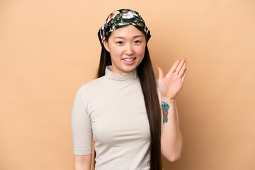 Young Chinese woman isolated on beige background saluting with hand with happy expression