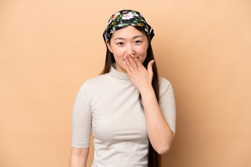 Young Chinese woman isolated on beige background happy and smiling covering mouth with hand