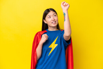 Young Chinese woman isolated on yellow background in superhero costume and celebrating a victory