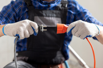 Hands of a man wearing work gloves hold an extension cord and cable connection of two plugs...