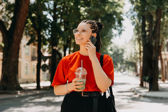 A photo of a young woman with box braids talking to her phone while holding a drink