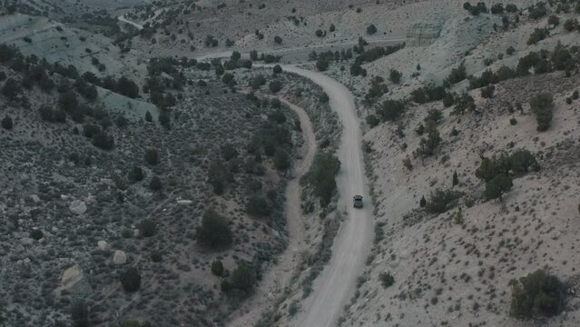 Drone shot of truck driving through desert. Drone shot of truck driving down dirt road. Vehicle driving on a dirt road. Driving in Utah mountains. Truck going through the mountains.