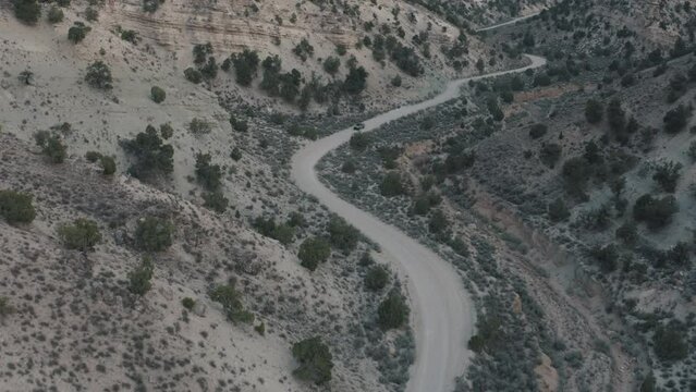 Drone shot of truck driving through desert. Drone shot of truck driving down dirt road. Vehicle driving on a dirt road. Driving in Utah mountains. Truck going through the mountains.