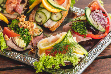 Danish traditional Smørrebrød or open sandwiches served in a plate, roast beef with remoulade, tomato and shredded horseradish on Danish rye bread, egg, prawns, lemon and mayonnaise