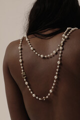 Close-up of beautiful woman back with pearl necklace on tan skin indoor. Mock-up