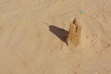 Beautiful sand castle with small Ukrainian flag on beach, space for text
