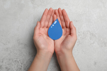 Save Water concept. Woman holding paper drop at light grey table, top view