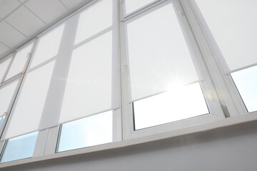 Large window with white roller blinds indoors, low angle view