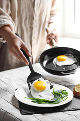 Woman putting tasty fried eggs onto plate at table indoors, closeup