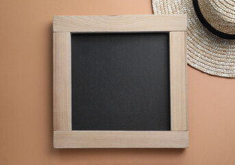 Blank chalkboard with straw hat on light brown background, flat lay. Space for text